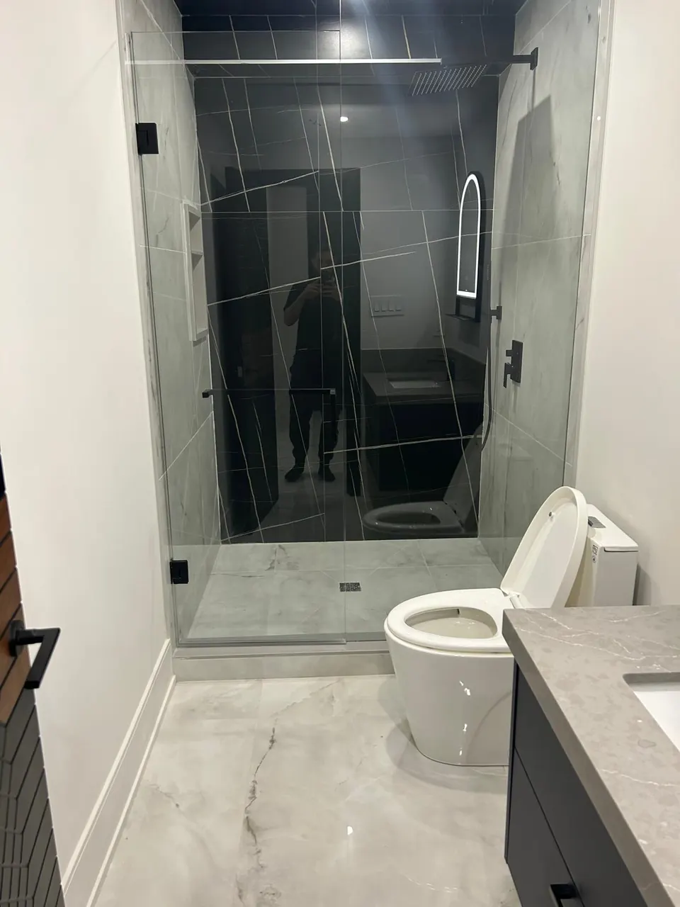 Glass shower with dark porcelain walls beside a floating vanity