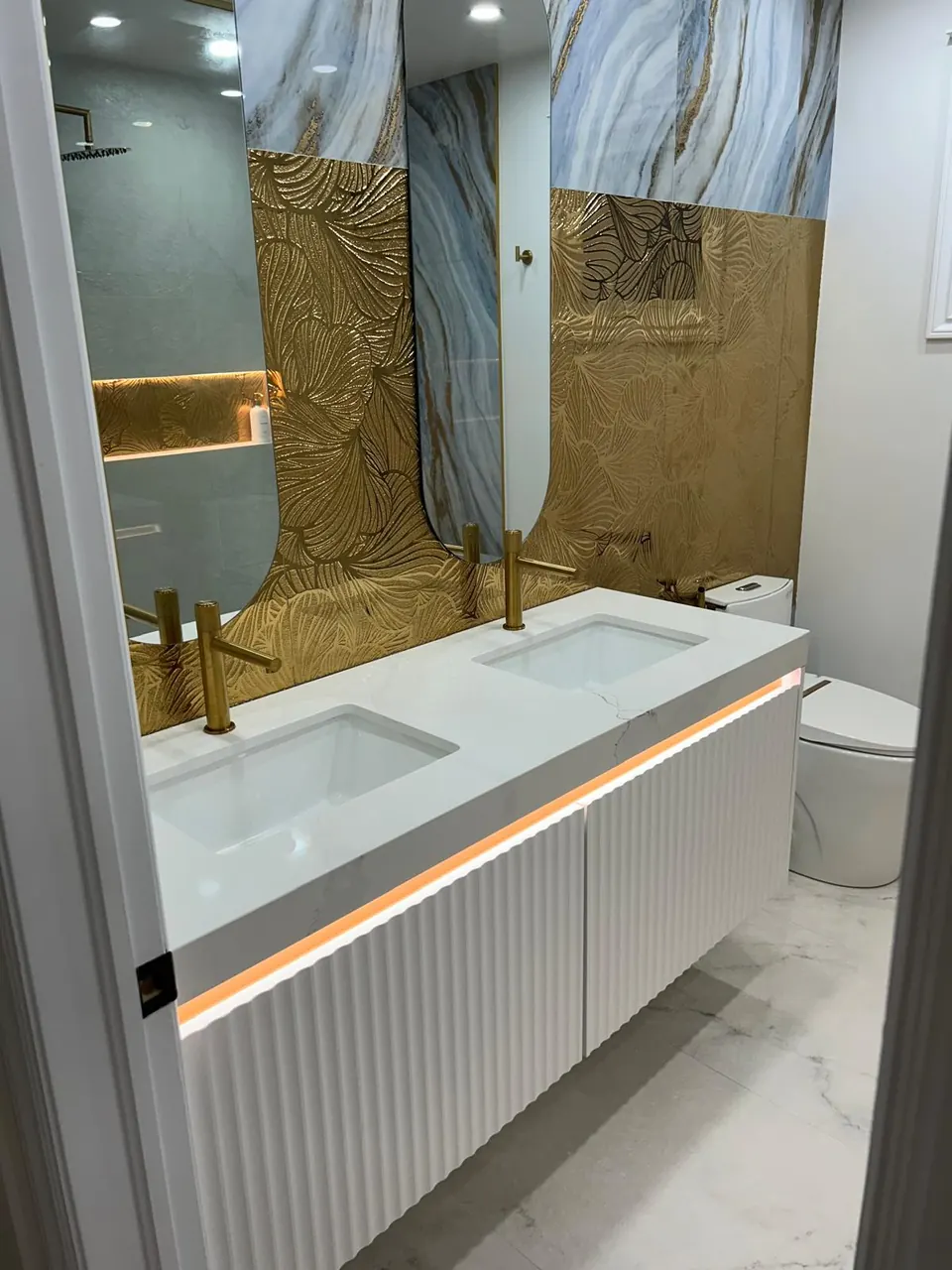 Floating fluted vanity with LED under-lighting and gold faucets