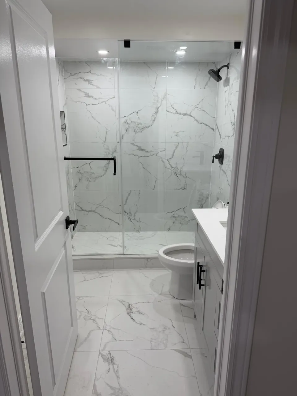 Glass shower with matte black fixtures next to a white vanity