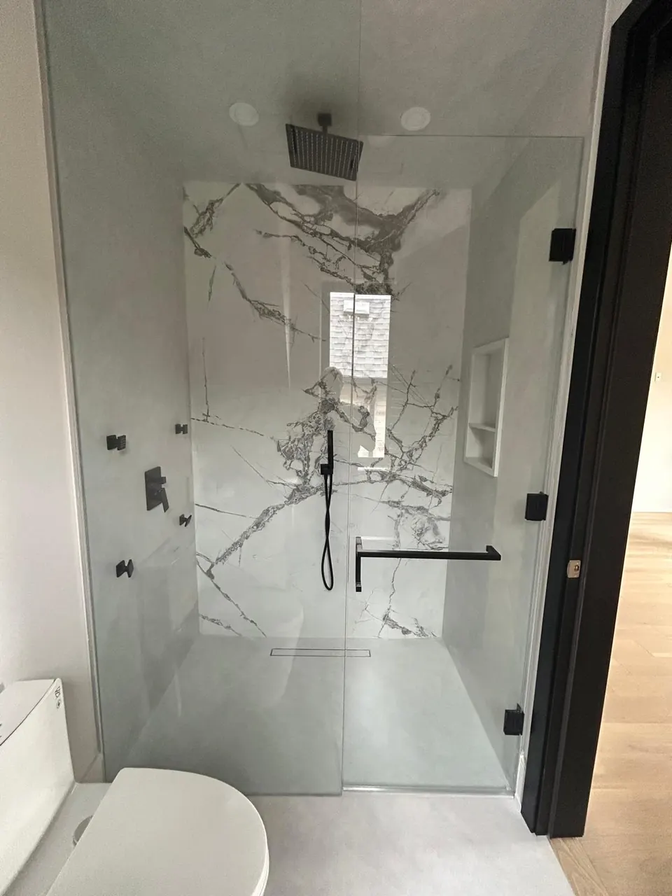 Walk-in glass shower with marble-look porcelain walls and matte black fixtures